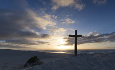 An old cross on sand dune next to the ocean with a calm sunrise