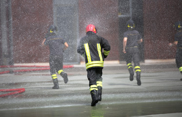 Firefighters run under the splashes of water during fire extingu