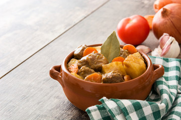 Beef meat stewed with potatoes, carrots and spices in ceramic bowl on wooden table
