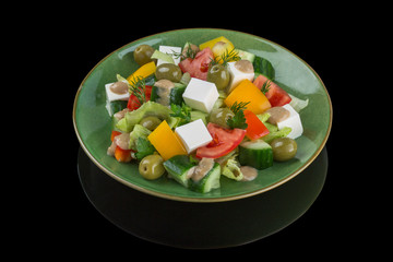Greek salad with fresh vegetables, feta cheese and black olives. Black background with reflection
