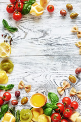 Fresh ingredients for italian lunch or dinner: uncooked tortellini, pasta, raw egg, cheese, tomato, basil and olives, lemon and pepper on white table. Food frame with copy space.