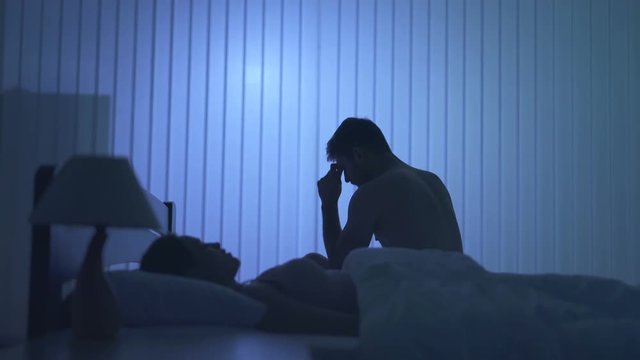 The nervous man sit near the woman on the bed. night time