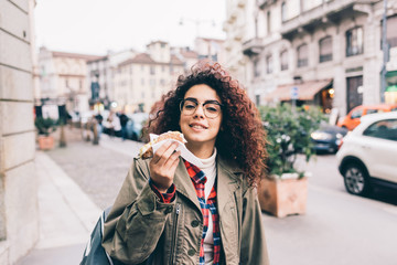 Fototapeta premium Young beautiful mixed race woman outdoor in the city eating cannolo - sweet, dessert, pastry concept
