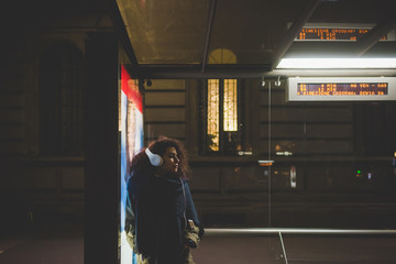 Young woman beautiful listening music at bus stop at night - transport, music, commuting concept