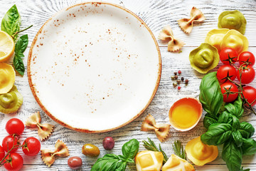 Italian meal food frame with empty plate. Tortellini, raw egg, fresh tomato and basil, olives, cheese, dry pasta on white background with copy space.