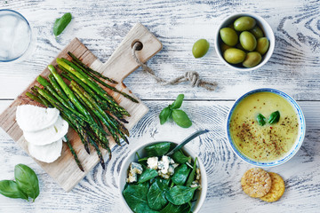 Baked asparagus with mozzarella, green puree soup, spinach salad with blue cheese and olives on white wooden table. Healthy green lunch or dinner concept. 