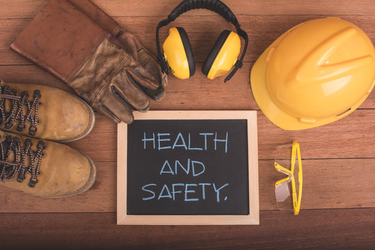 Standard construction safety equipment on wood background with health and safety text on blackboard.