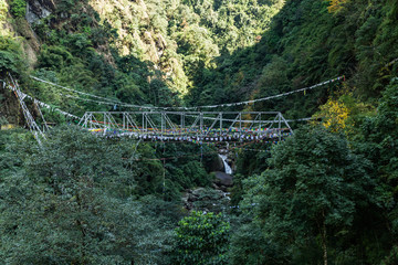 Tibetan Buddhist Prayer Flag include red, green, yellow, blue and white colors swaddle bridge and trees in Sikkim, India.
