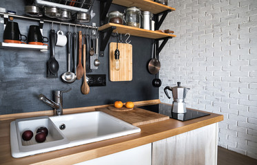 Design of a modern home kitchen in the attic and rustic style. Black wall with shelves, trays, jars, mugs, sink. In the background a wall of white brick.