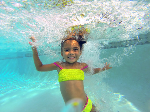 little girl swiming underwater in a pool posing to camera 
