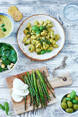 Top view of healthy green lunch or dinner concept. Gnocchi with pesto, spinach salad, baked asparagus with mozzarella, green puree soup and olives on white table. 