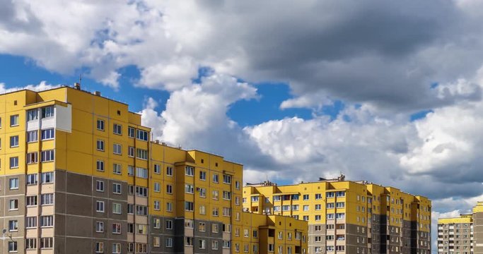 Time lapse clip of white fluffy rolling clouds against the background of yellow multi-storey apartment buildings