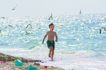 boy running at the beach with seagulls behind him 