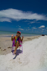 girl sitting in chair at the beach playing to camera 