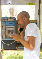 Young bald man talking in the old phone box