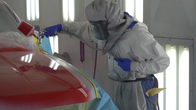 Auto bodyshop painter paints and varnishes a truck with red lacquer