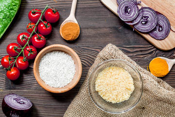 rice, spices and vegetables for paella on wooden desk background top view