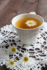 White cup with infusion of tea from daisies on a dark wooden table concept of a healthy herbal vegetable drink