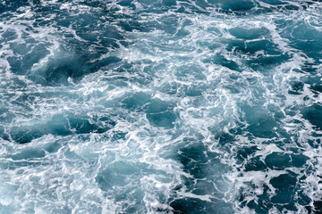 Natural background of blue-green sea water with foam and waves.