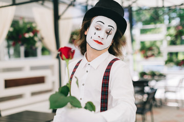 Emotional male mime artist with red rose posing on the summer terrace at the restaurant