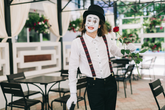 Emotional male mime artist with red rose posing on the summer terrace at the restaurant