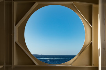 View of the ocean on a clear blue sky day thru an open window on a cruise ship