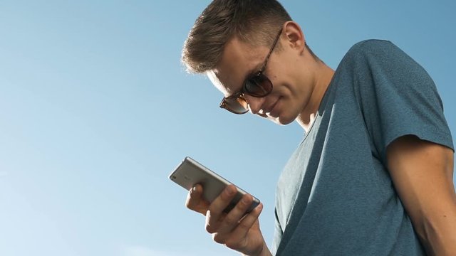 Man wears sunglasses texting message on smartphone on the city street, urban technology concept