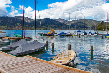 Fototapeta na wymiar Sailing boats at the jetty in the tegernsee lake, blue sky with clouds in the background, landscape in the tourist resort bavarian alps, bavaria, germany, landscape