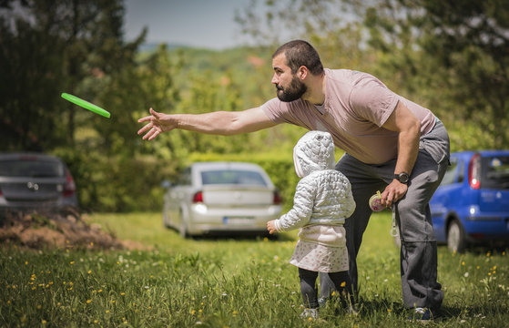 Young Dad And His Little Daughter Playing Frisbee In The Park