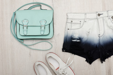 Mint handbag, denim shorts, sneakers. Fashionable concept. Wooden background