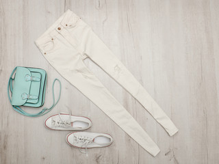 White jeans and sneakers, mint bag. Fashionable concept. Wooden background.