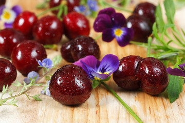 Cherries on wooden table with water drops macro background. With wildflowers. Closeup. 