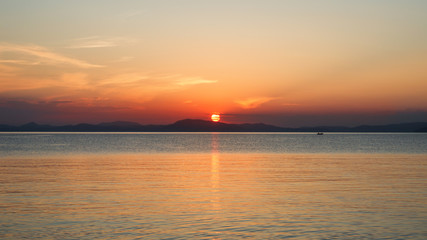 Glanzvoller Sonnenuntergang am Meer mit Sonnenspiegelung und kleinen Boot