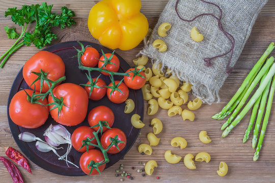 Concept of italian cuisine, vegetarian, healthy food. Ingredients for italian food, dry pasta, vegetables, tomatoes, garlic, asparagus, bell pepper, wooden background