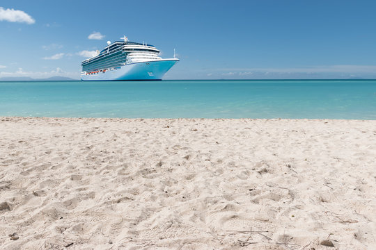 Summer tropical cruise vacation concept.
White Caribbean sandy beach with luxury cruise ship in the background