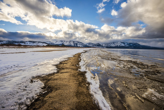A view looking down Commons Beach in the winter with a dramatic sunset overhead in South Lake Tahoe, California.