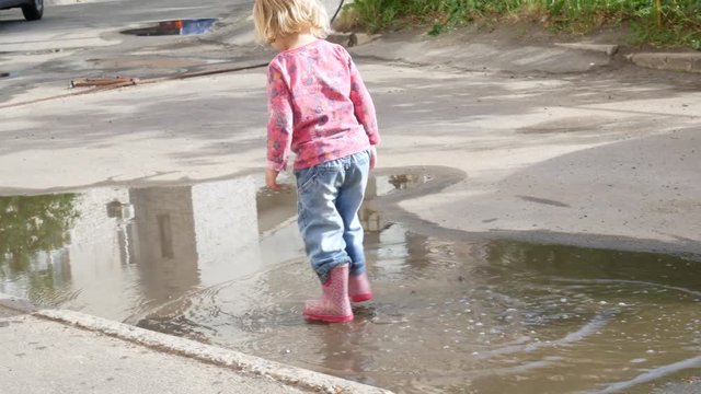 A dirty puddle, a child jumping in it. The girl walks in a puddle.