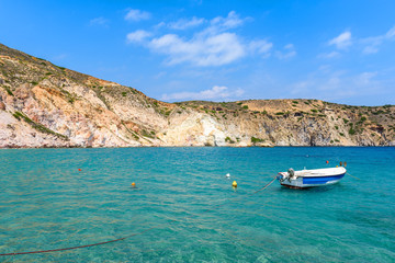 Naklejka na ściany i meble White boat anchoring in beautiful Firopotamos bay with emerald green sea water, Milos, Cyclades Islands, Greece.