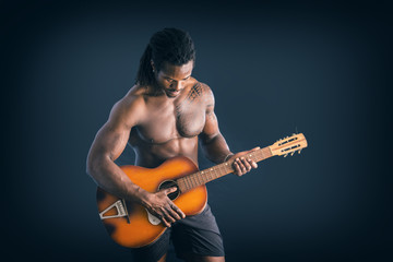 Portrait of muscular topless young black man playing guitar on dark background