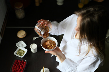 Young woman pouring granola into a bowl, breakfast, healthy food