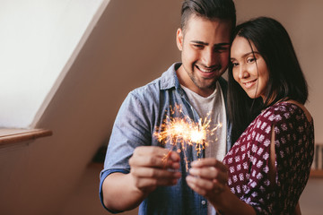 Loving young couple celebrating with sparklers at home
