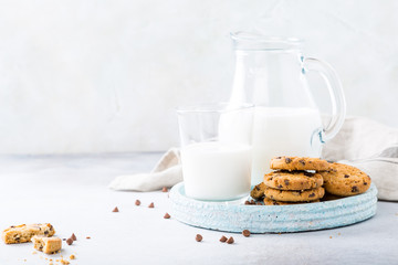 Stack of chocolate chip cookies on blue stone plate with glass of milk on light gray background. Selective focus. Copy space.