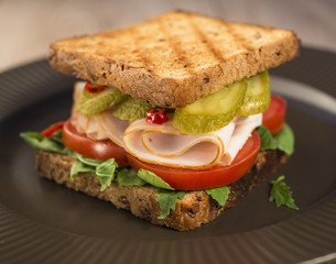 Sandwich with tomatoes, ham salted cucumber on a brown plate.