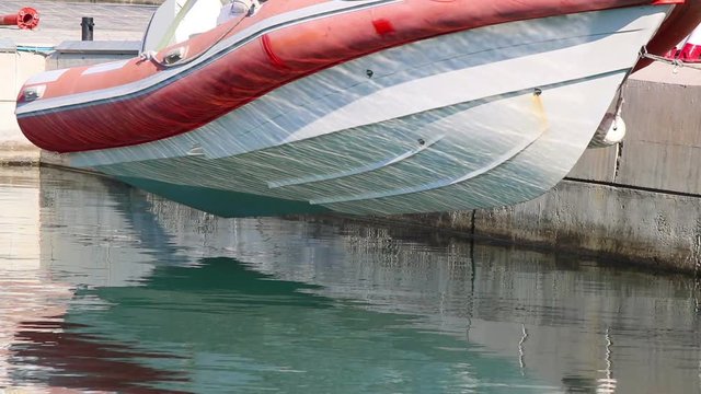 A boat hanging on a crane above water with wave reflections on its hull