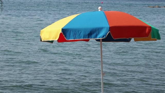 A typical colorful beach umbrella on the wind with sea waves on the background, for touristic and travel concepts