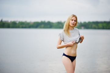 Portrait of a fantastically looking tall model wearing t-shirt and bikini walking in lake.