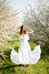 Fototapeta premium Beautiful young girl in white dress and wreath of flowers on head in blooming gardens