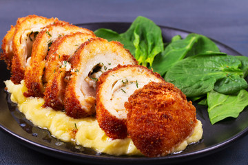Chicken Kiev on mashed potato with spinach. Breaded chicken breast stuffed with herbs and butter on black plate