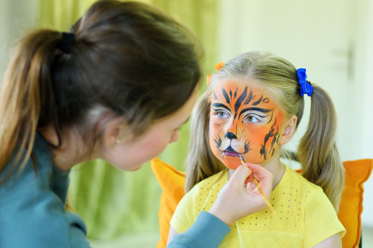 Adorable little girl getting her face painted like tiger by artist