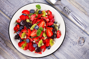 Strawberry, blackberry, blueberry and kiwi salad, garnished with mint. Fruit and berry salad. View from above, top studio shot